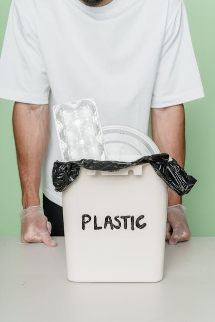 A person wearing a white T-shirt and transparent disposable gloves is standing behind a white plastic container labeled 'PLASTIC,' which is used for waste sorting or recycling. The container has a hin