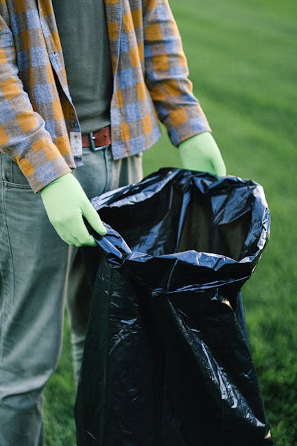 A person wearing a white T-shirt and transparent disposable gloves is standing behind a white plastic container labeled 'PLASTIC,' which is used for waste sorting or recycling. The container has a hin